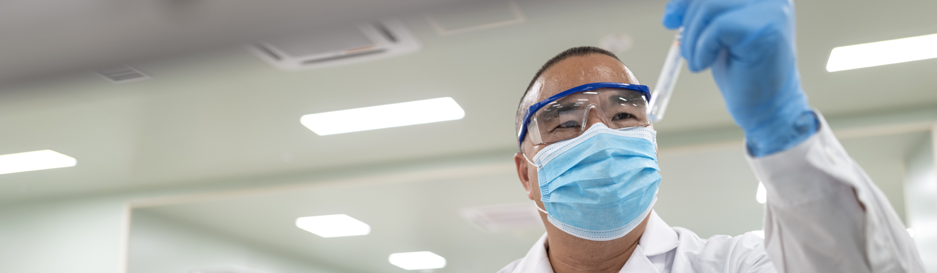 Masked researcher looks at a test tube